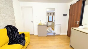 Ein kompakter Wohnbereich mit gelbem Sofa, schwarzer Decke, einer Küchenzeile und einem kleinen Badezimmer.