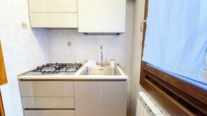 Una cocina compacta con estufa a gas, un lavamanos y una ventana con cortina.