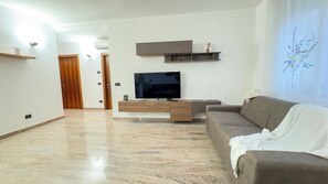 Ein modernes Wohnzimmer mit Flachbildfernseher, Couchtisch aus Holz, braunem Sofa und einer Wanddekoration.