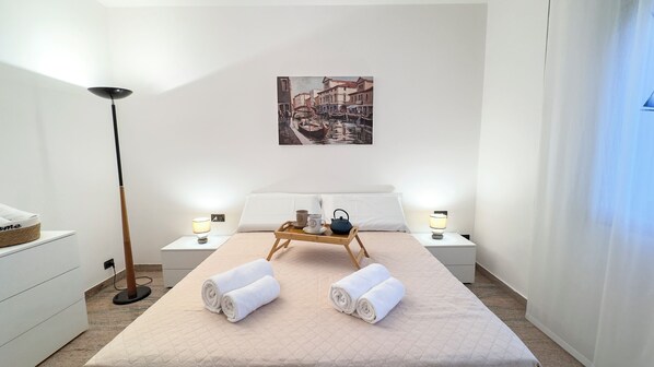 A hotel room with a bed, two bedside tables with lamps, a tray with towels and a teapot, and a painting on the wall. - Casa Micio by Ca-sa Check (Chioggia)