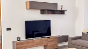 A modern living room with a flat-screen TV, wooden furniture, and built-in shelves. - Casa Micio by Ca-sa Check (Chioggia)