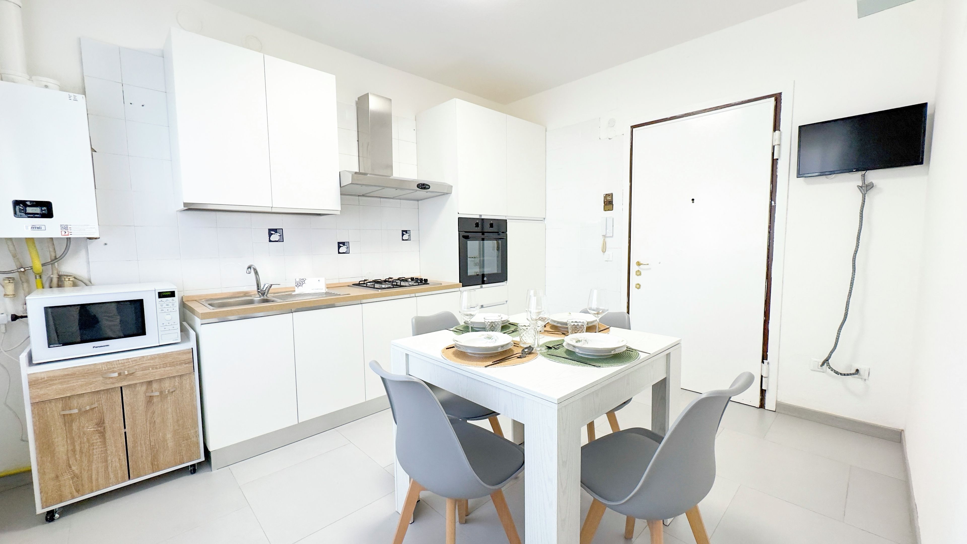 A modern kitchen with white cabinets, a microwave, an oven, and a dining table set with plates and glasses.