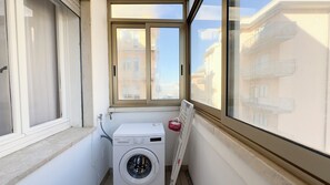 A laundry area with a washing machine and dryer, a window with a view of buildings, and a radiator. - Appartamento Madagascar by Ca-sa Check (Chioggia)