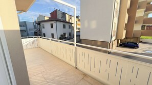 Ein Balkon mit beiger Brüstung, gefliestem Boden und Blick auf umliegende Gebäude sowie ein parkendes Auto.