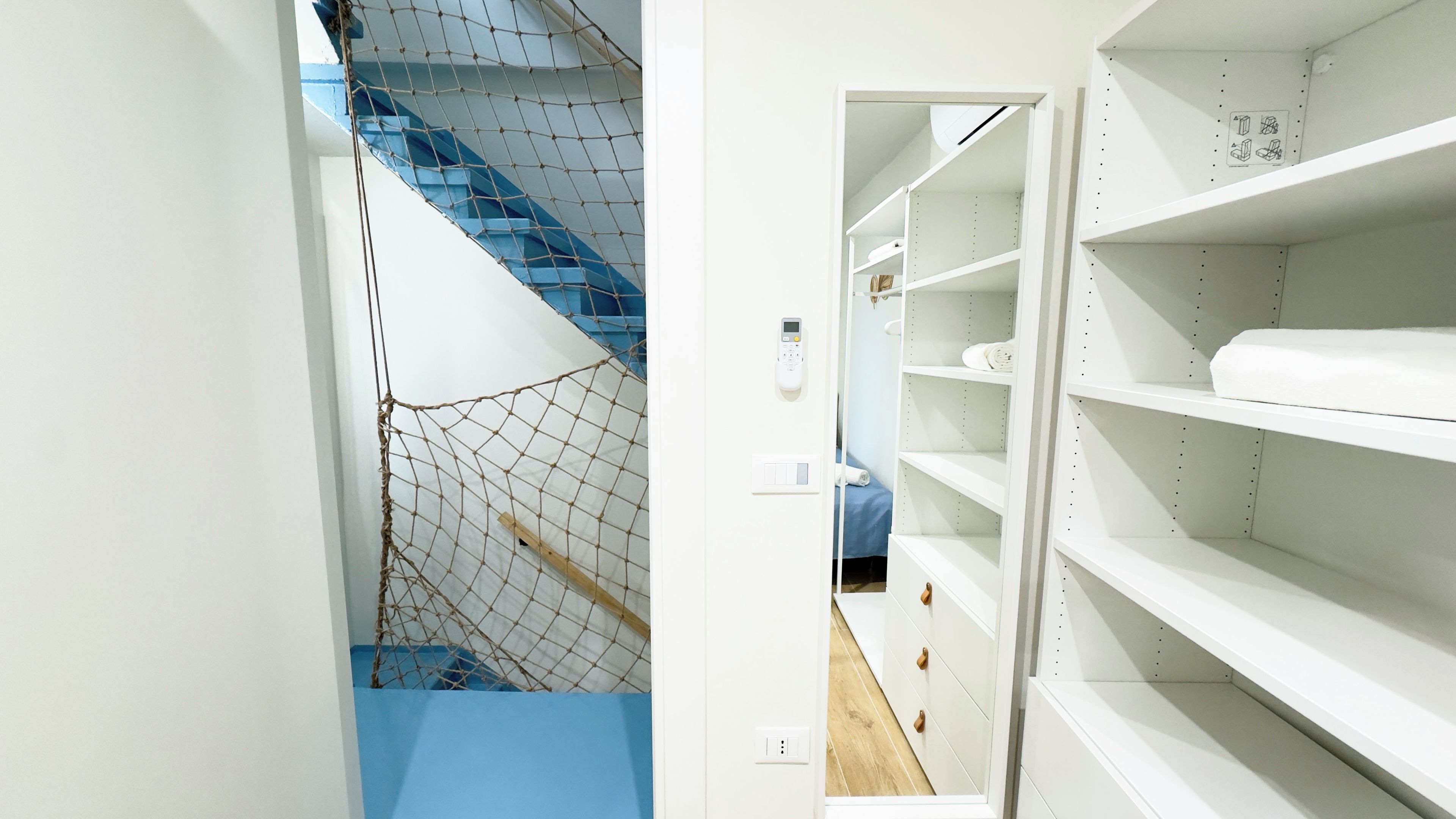 A room with a staircase, a white wardrobe, and a blue wall.