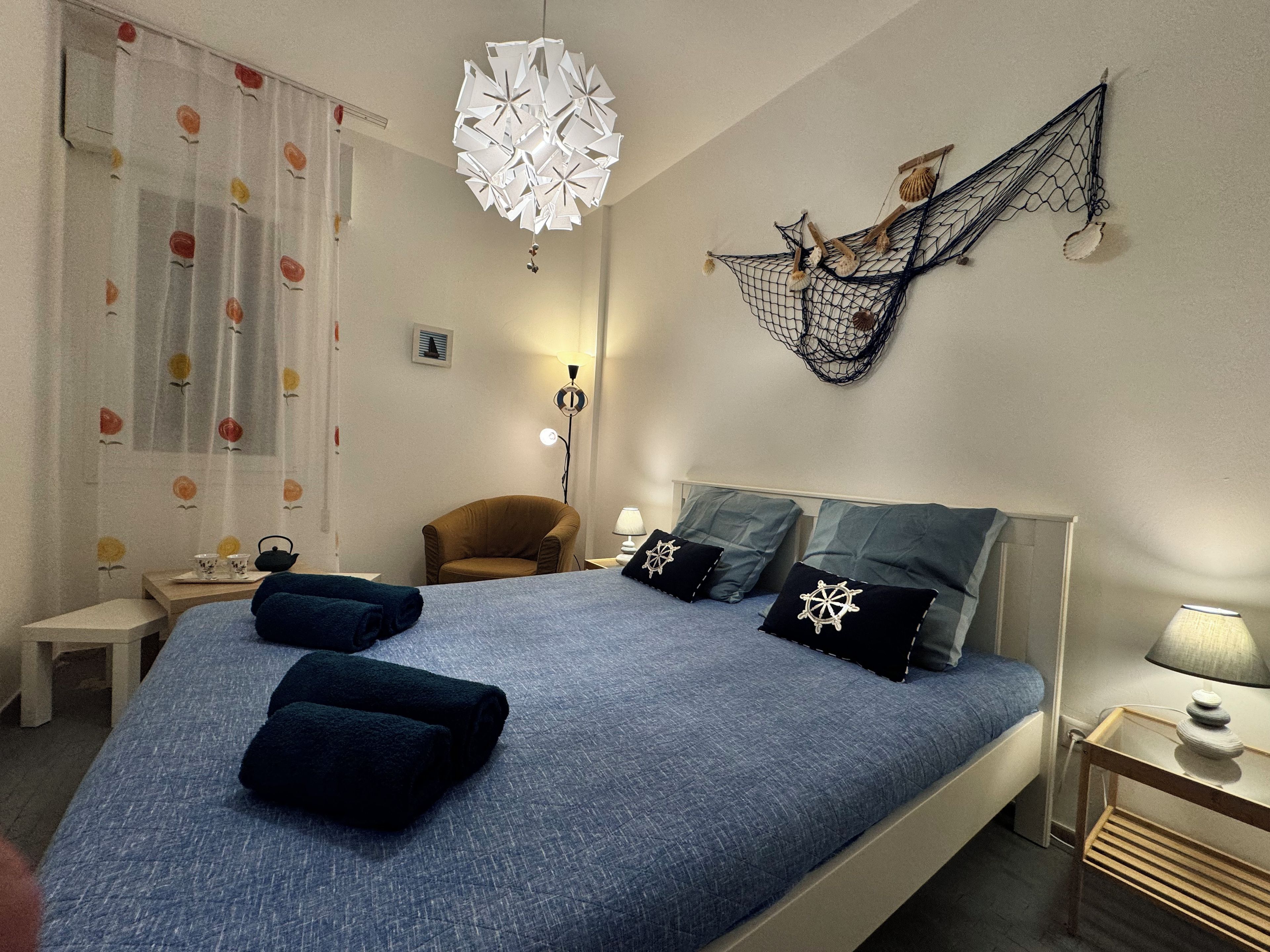 Un dormitorio con cama, almohadas, una silla, escritorio, lámpara y decoración en la pared.