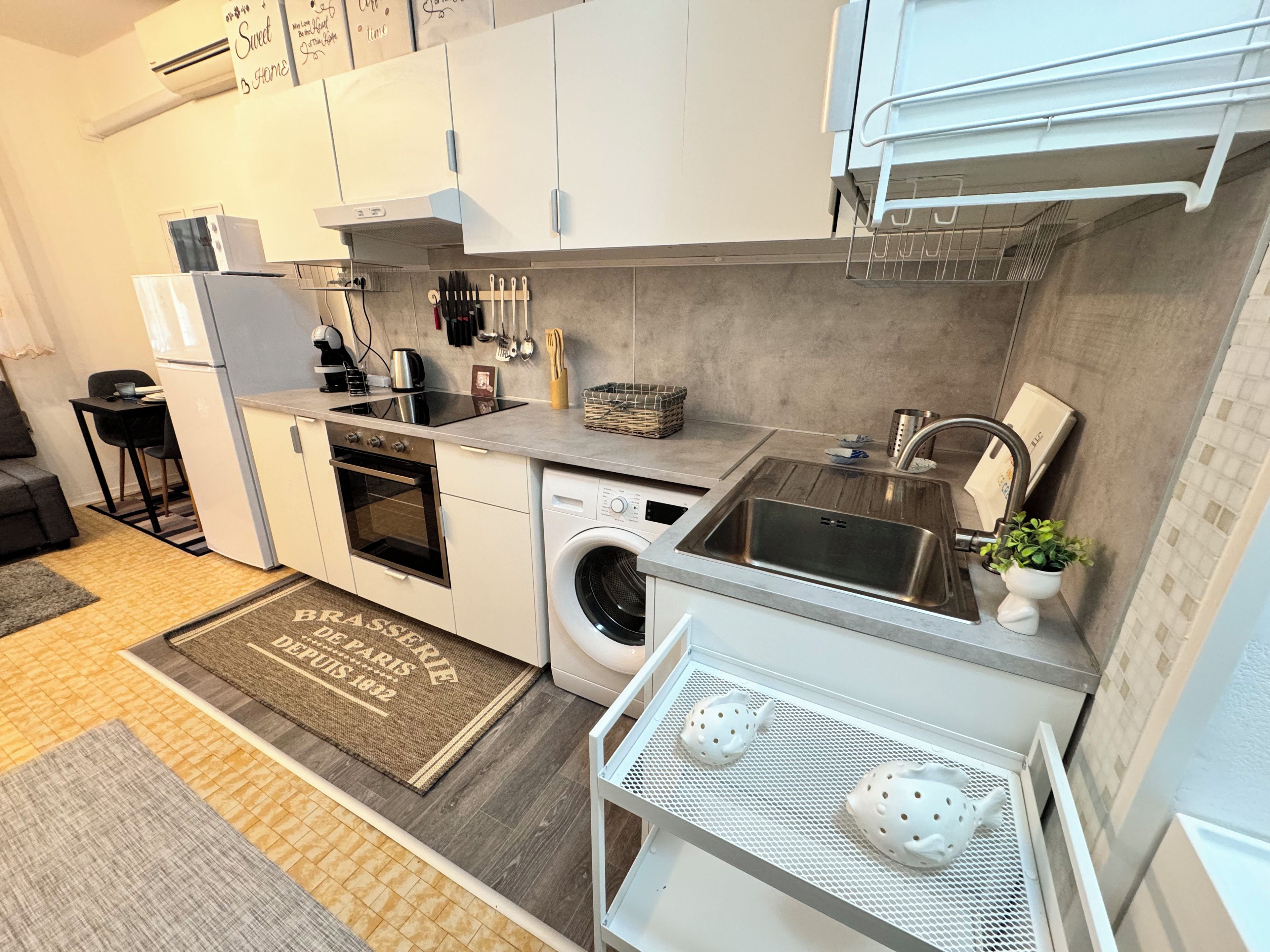 A compact kitchen with white cabinets, a built-in oven, a washing machine, and a sink.