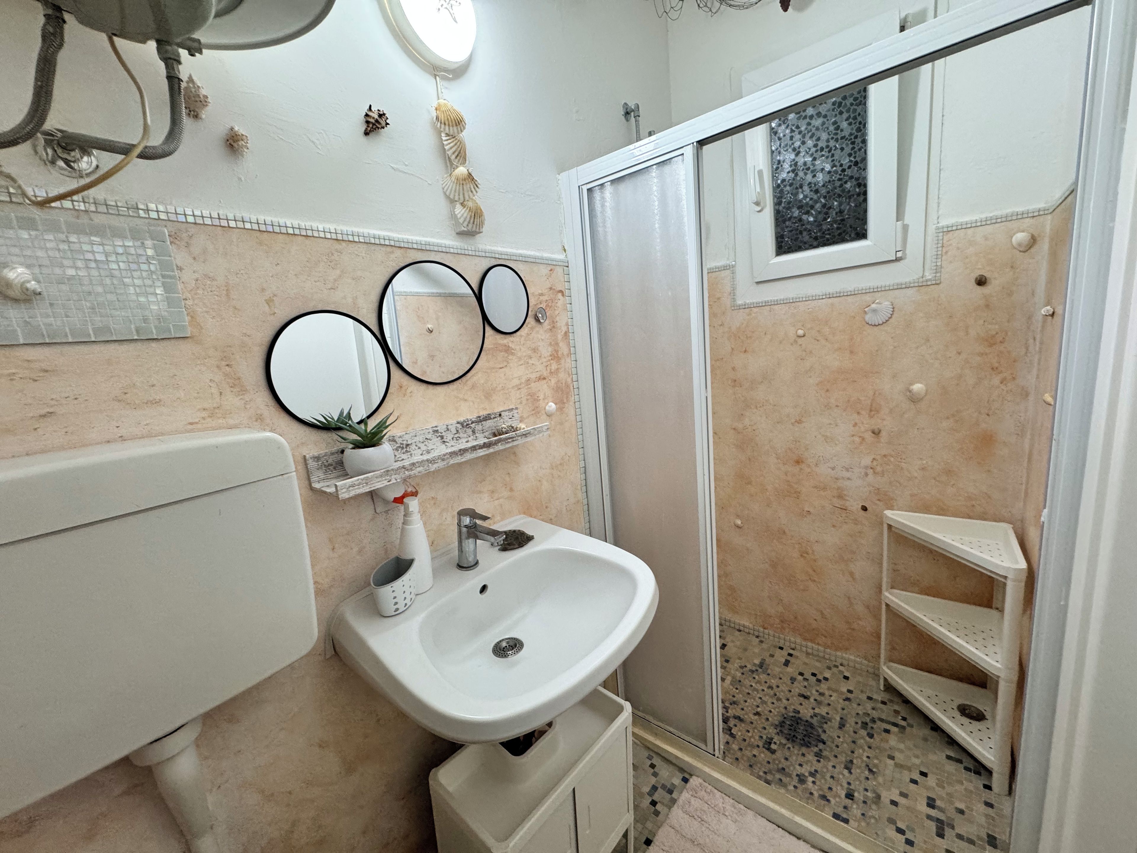Casa de banho com lavatório, espelho, chuveiro e paredes revestidas a azulejos.