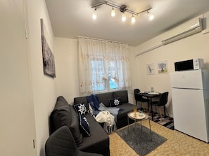 Un espacio habitable compacto con sofá, mesa de comedor y kitchenette.