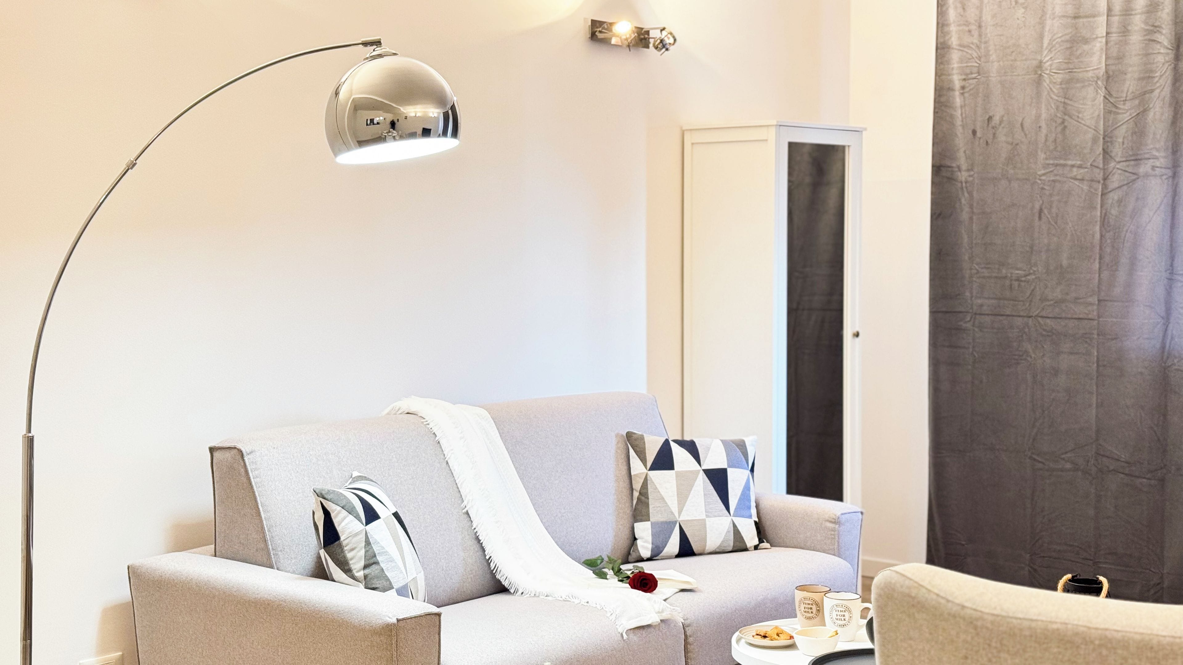 A modern living room with a sofa, a side table with a tray of food, a floor lamp, and a large mirror.