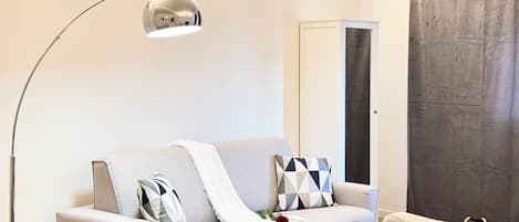 Ein modernes Wohnzimmer mit einer Couch, einem Beistelltisch mit Speisen und einer stehenden Lampe sowie einem großen Spiegel.