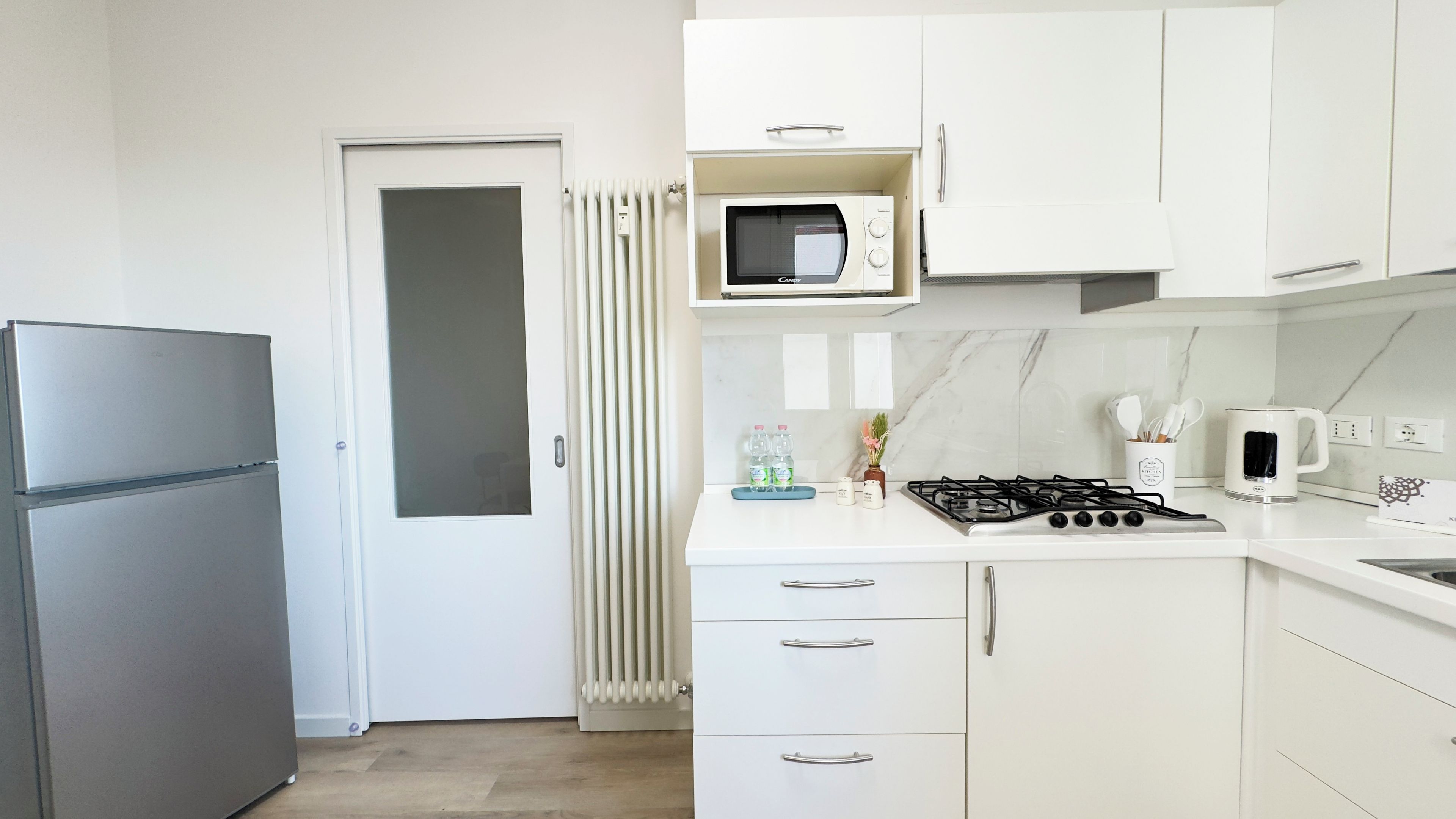 Una cocina moderna con refrigerador, microondas, estufa y gabinetes blancos.