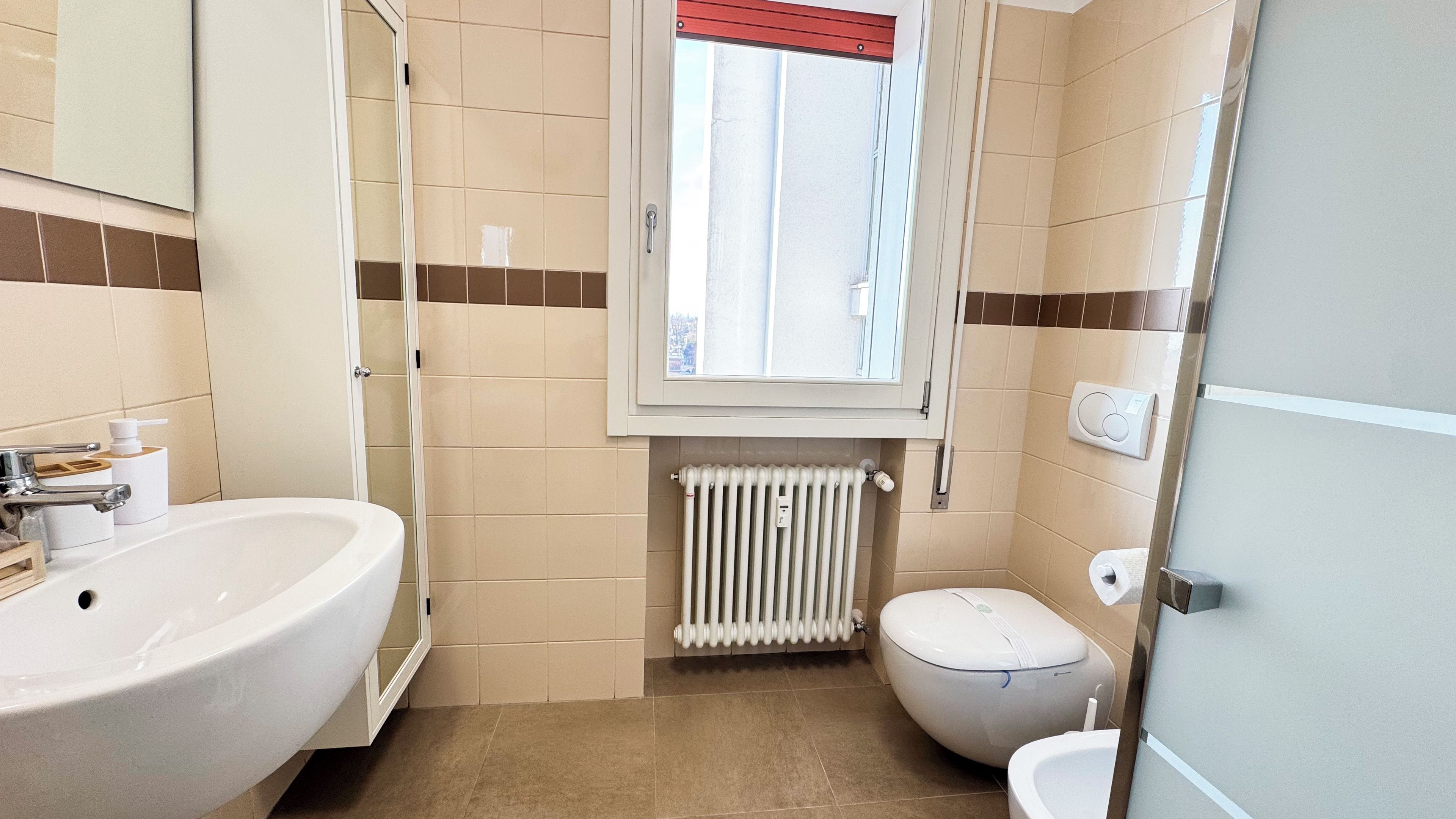 Un bagno con lavandino, WC e finestra.
