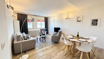 Ein modernes Wohnzimmer mit Sofa, Fernseher und Essbereich mit Stühlen und Tisch.