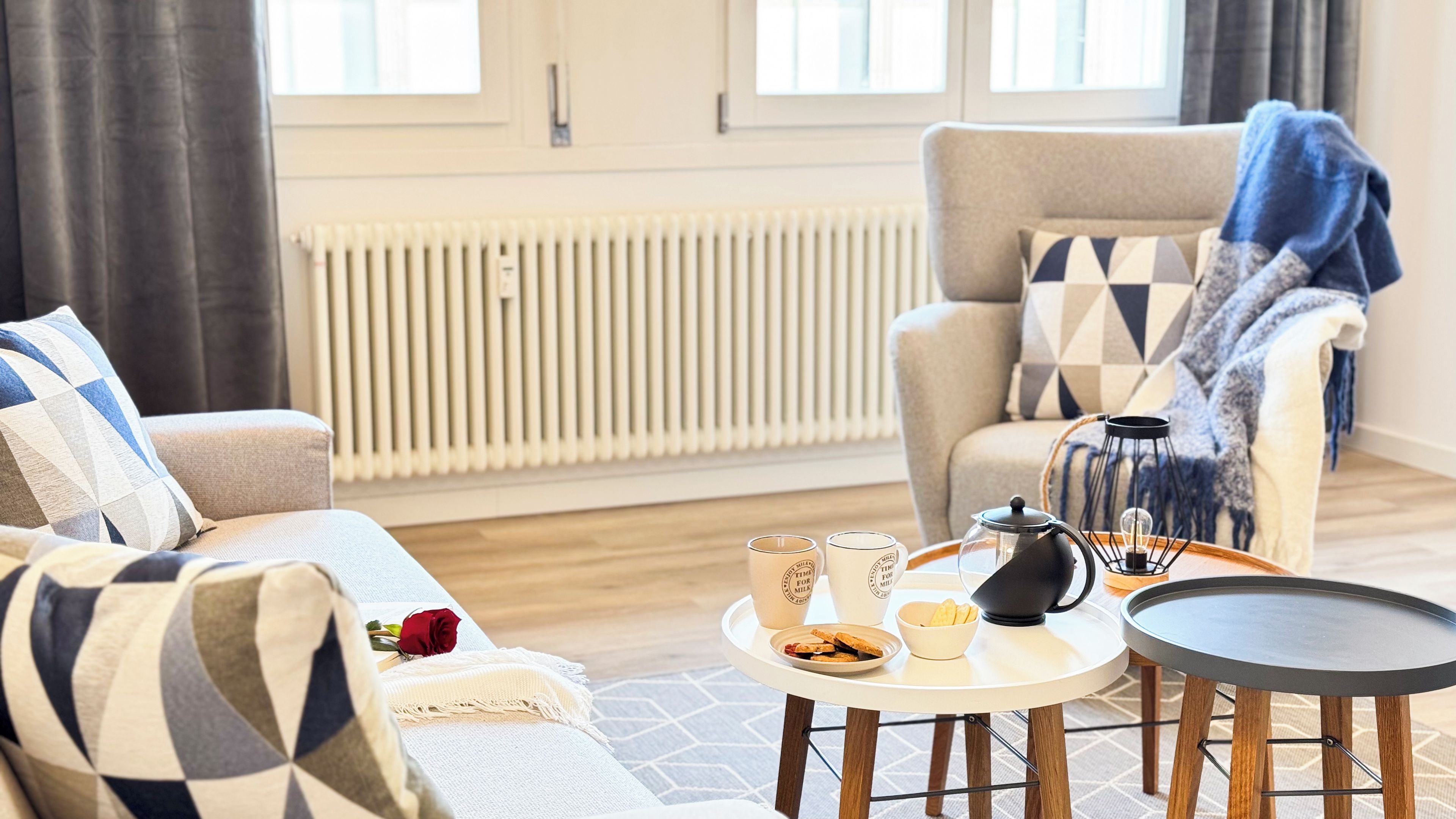 A living room with a sofa, armchair, coffee table, and a radiator.