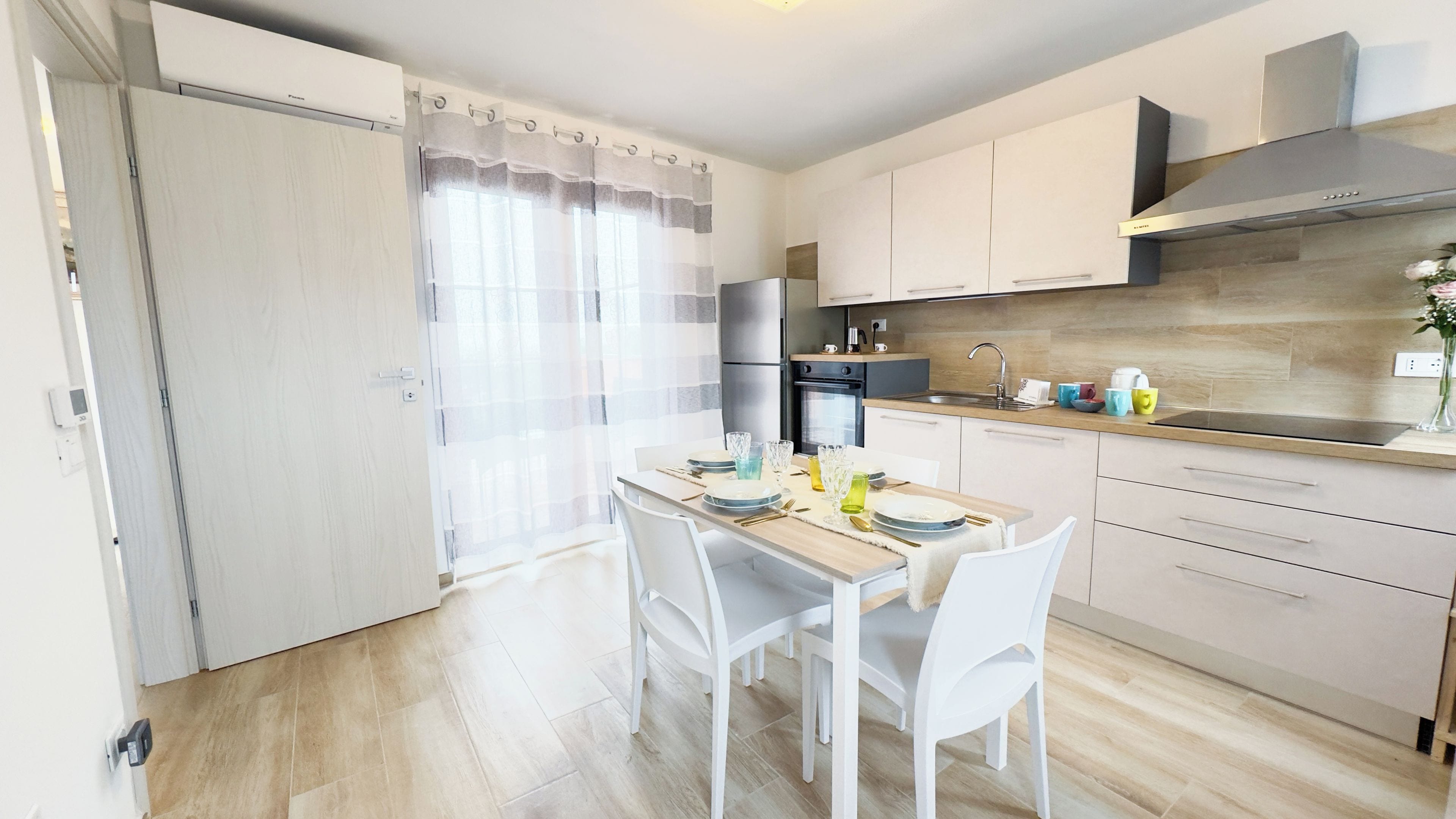 A modern kitchen with white cabinets, a stainless steel range hood, and a dining area with a table set for four.