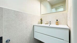 Um banheiro moderno com toucador branco, espelho e parede revestida de azulejos.