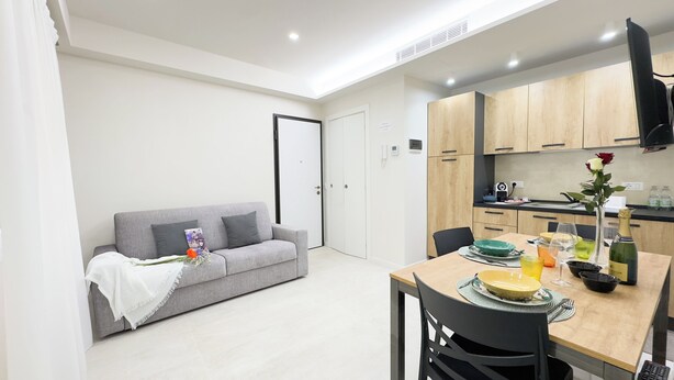 Um espaço de estar compacto com cozinha compacta, área de jantar e sofá cinza com almofada decorativa.