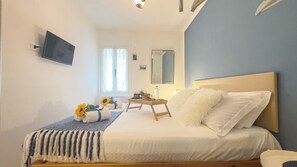 Un dormitorio con una cama, una mesita de noche, un espejo y un televisor en la pared.
