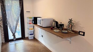 Een compacte keuken met een magnetron, koffiezetapparaat en een klein plankje met decoratieve spullen.