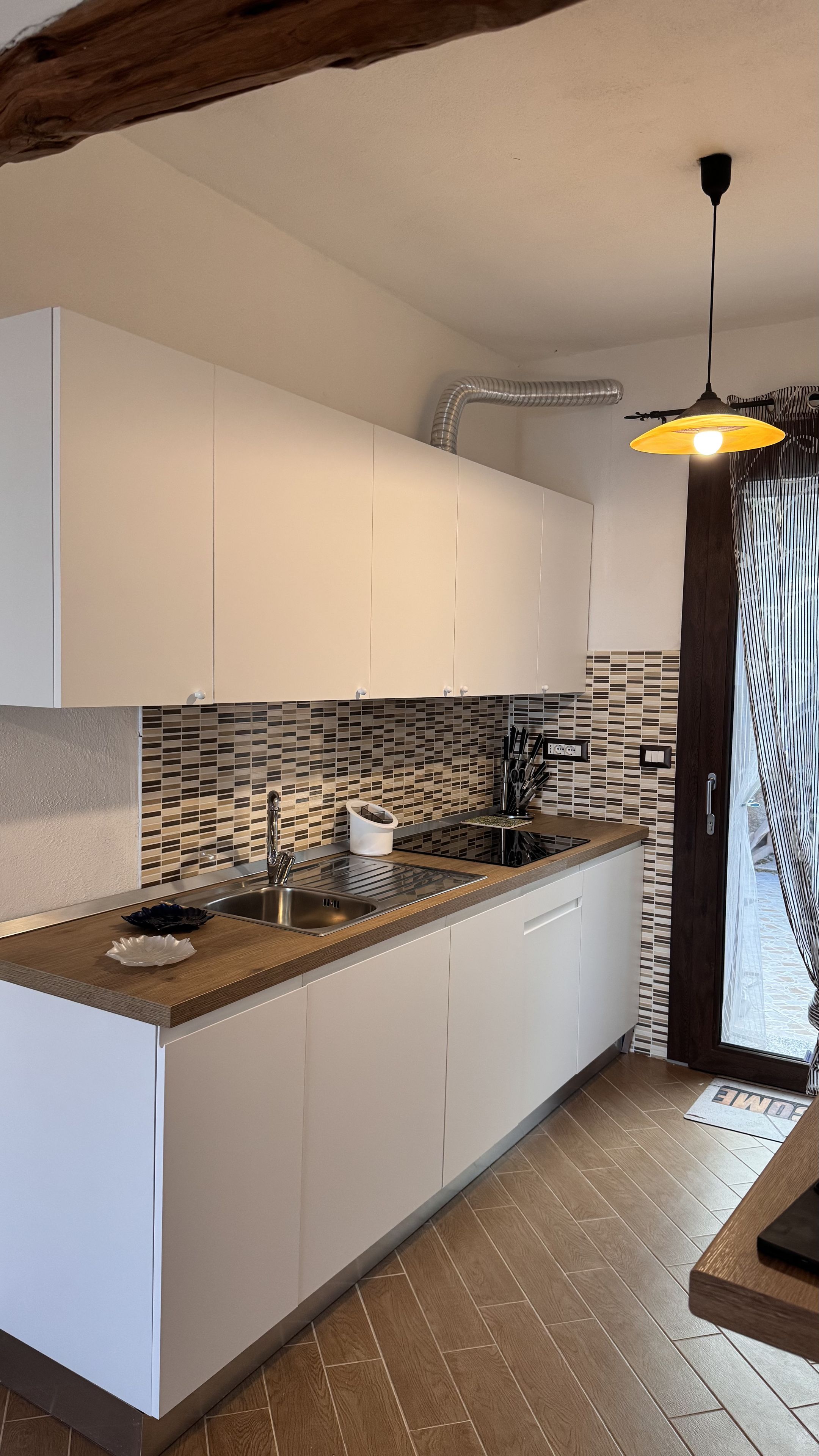 A modern kitchen with white cabinets, a wooden countertop, a sink, and a hanging light fixture.