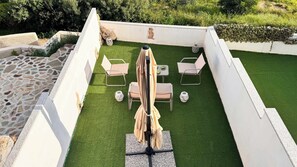 Een terras met een tafel en stoelen, omgeven door witte muren en een stenen vloer.