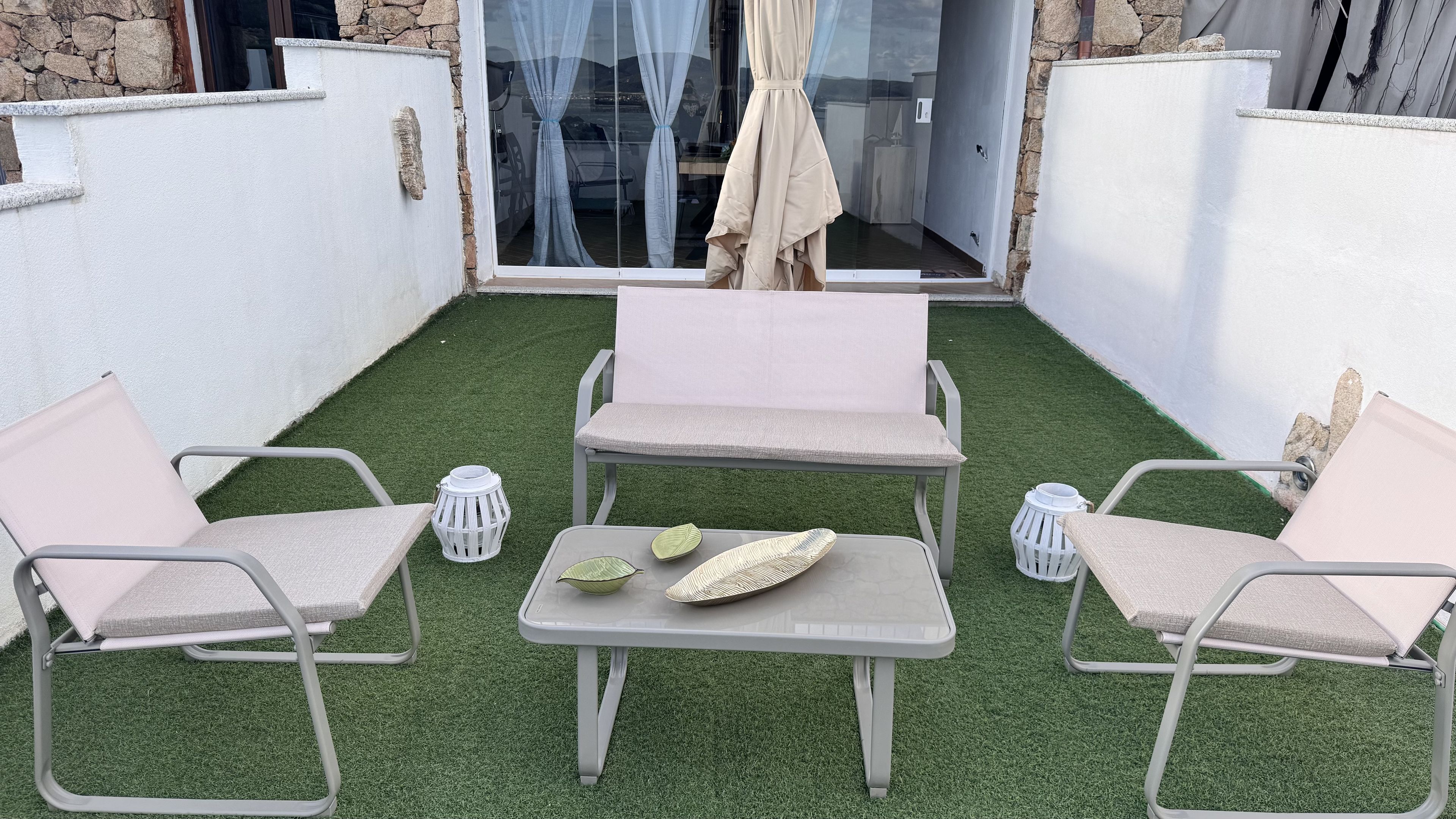 A patio with artificial grass, two cushioned chairs, a small table, and a white lantern.