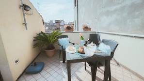 A small outdoor balcony with a table set for two, featuring a potted plant, a vase with flowers, and a plate of food. - Casa Andrea by Ca-sa Check (Chioggia)