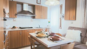 A modern kitchen with wooden cabinets, a stainless steel range hood, and a dining area with a table set for two. - Casa Andrea by Ca-sa Check (Chioggia)