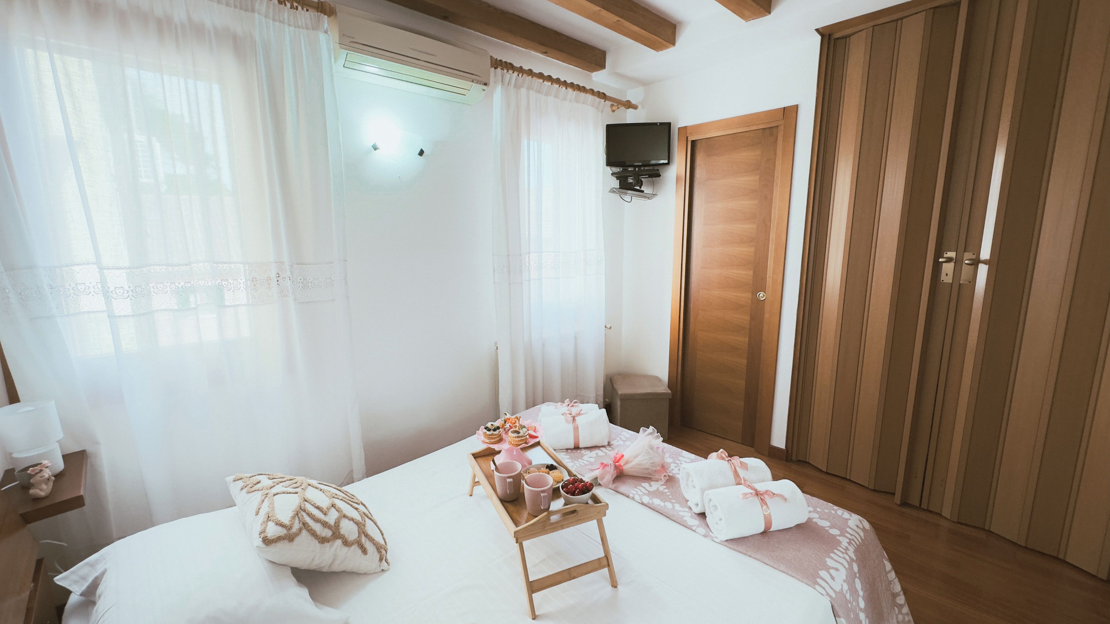 A bedroom with a bed, bedside table, curtains, a wooden wardrobe, and a small wooden stool with items on it.