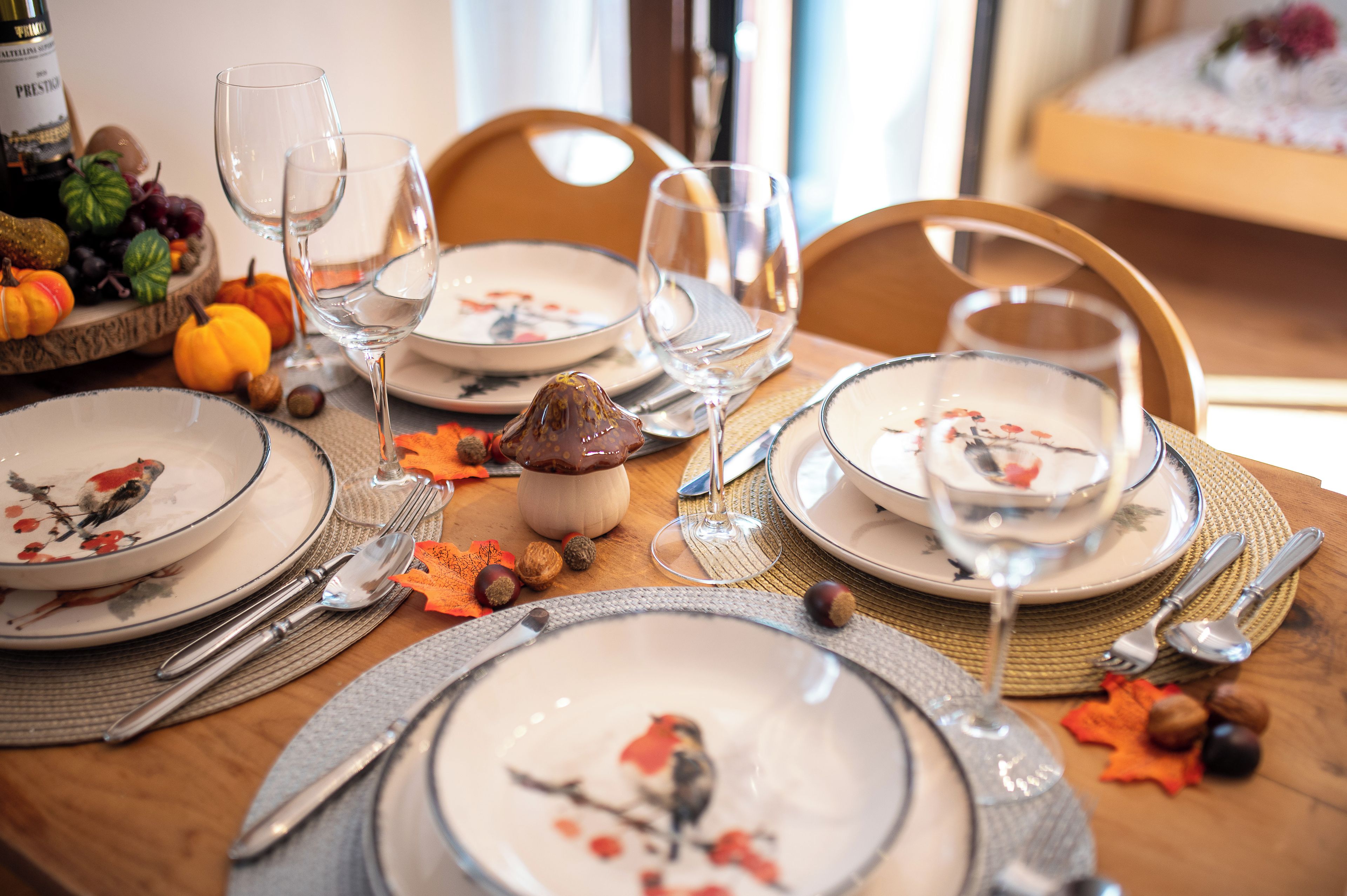 Una mesa de comedor preparada con platos, cubiertos y copas de vino, rodeada de adornos con motivos otoñales.