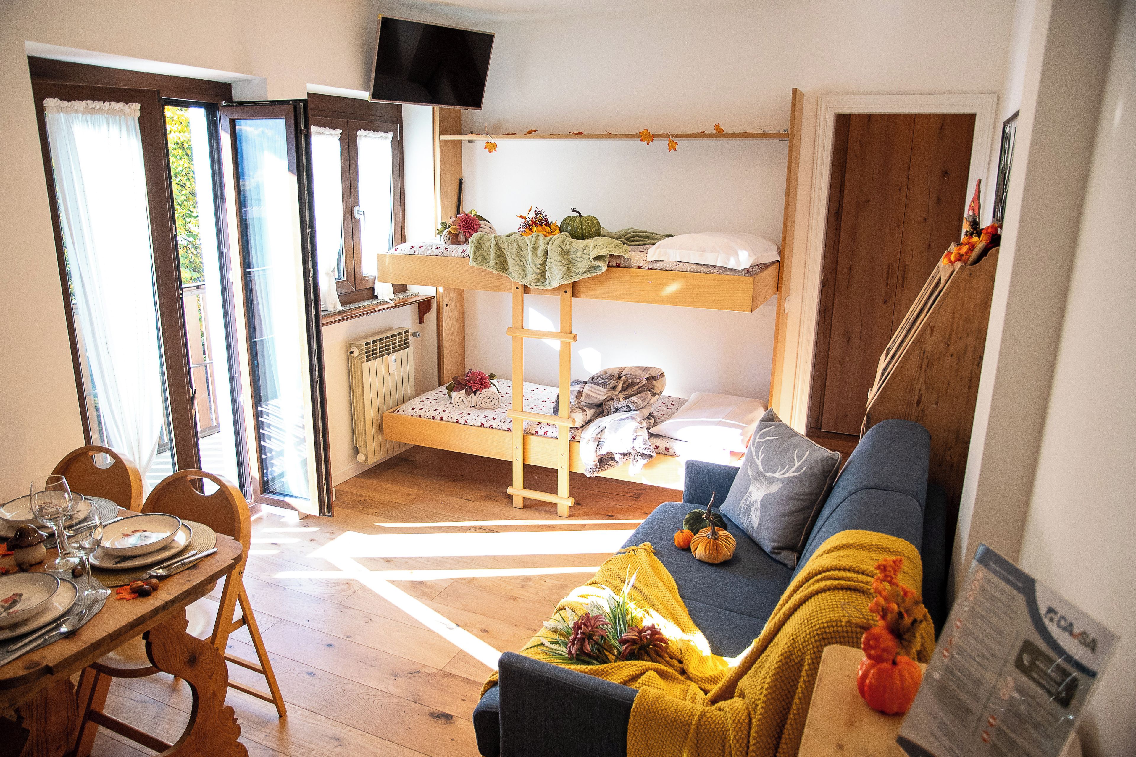 Ein gemütliches Zimmer mit einem Etagenbett, einer Schlafcouch, einem Esstisch für vier Personen und einem an der Wand befestigten Fernseher.