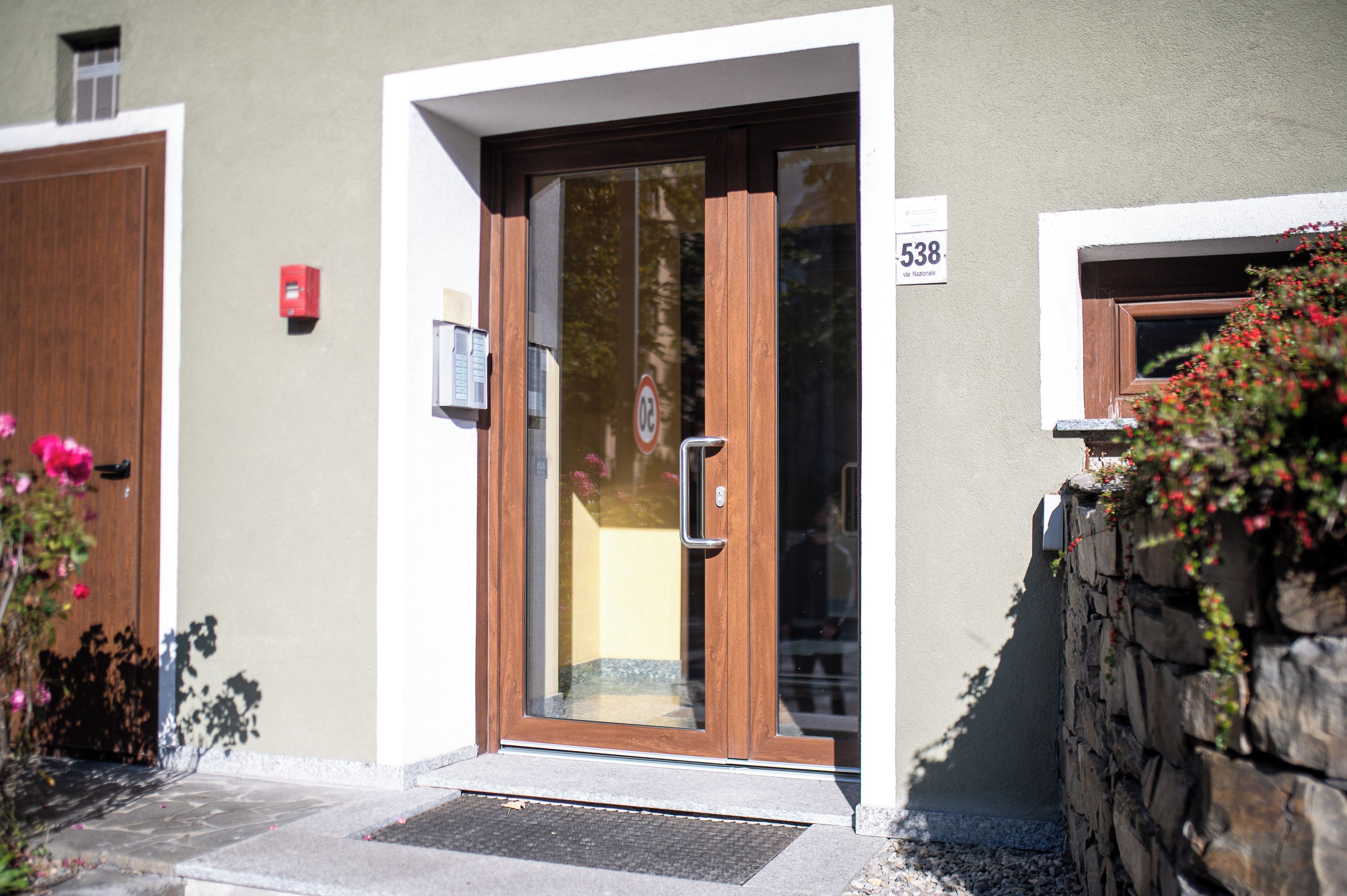 A building entrance with a wooden door, a mailbox, and a stone wall with plants.