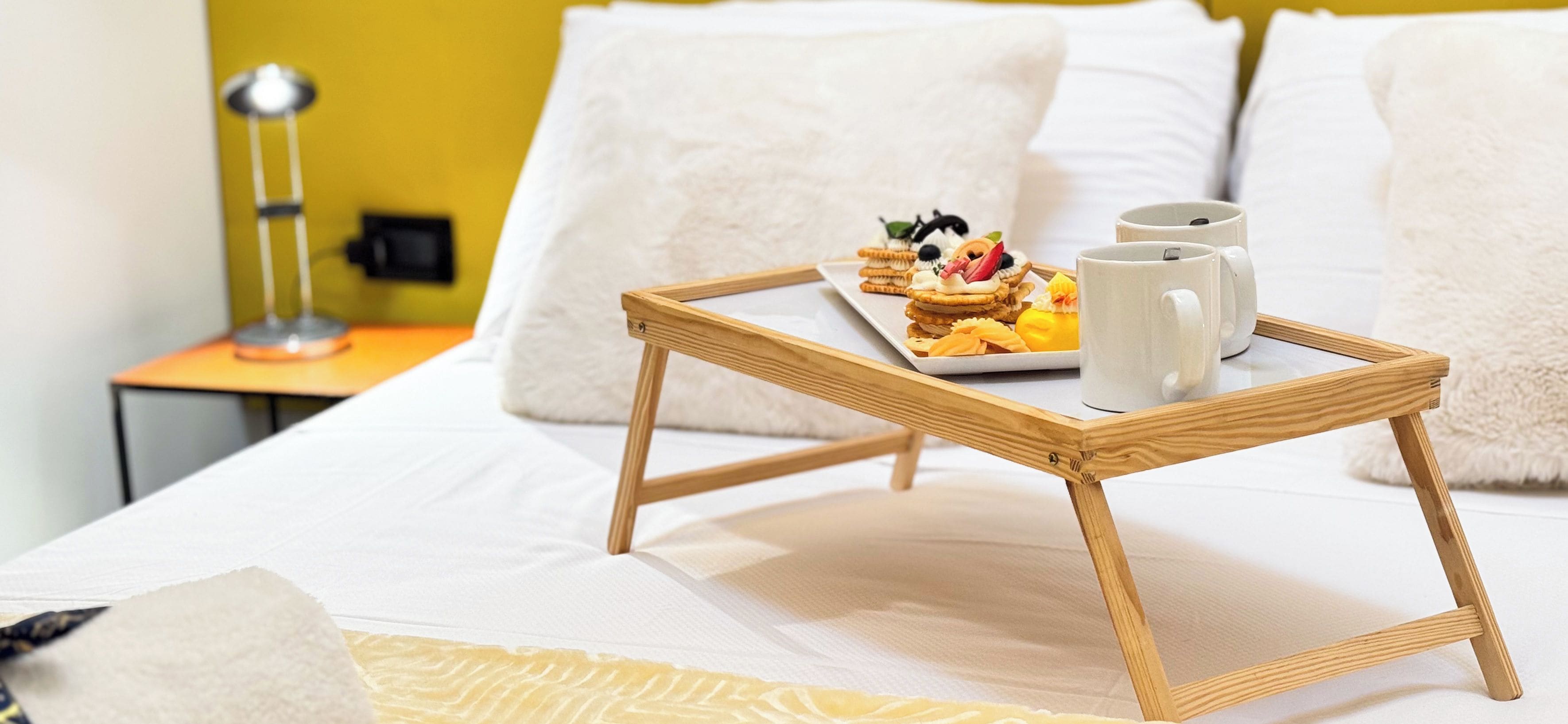 Una cama con una bandeja de comida y dos tazas sobre un atril de madera.