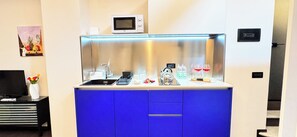 Una kitchenette compacta con microondas, lavamanos y armarios azules.