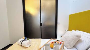 Une chambre d’hôtel avec un lit, une table de chevet sur laquelle se trouve un plateau de petit-déjeuner, une serviette et une porte dont les panneaux sont en verre dépoli.