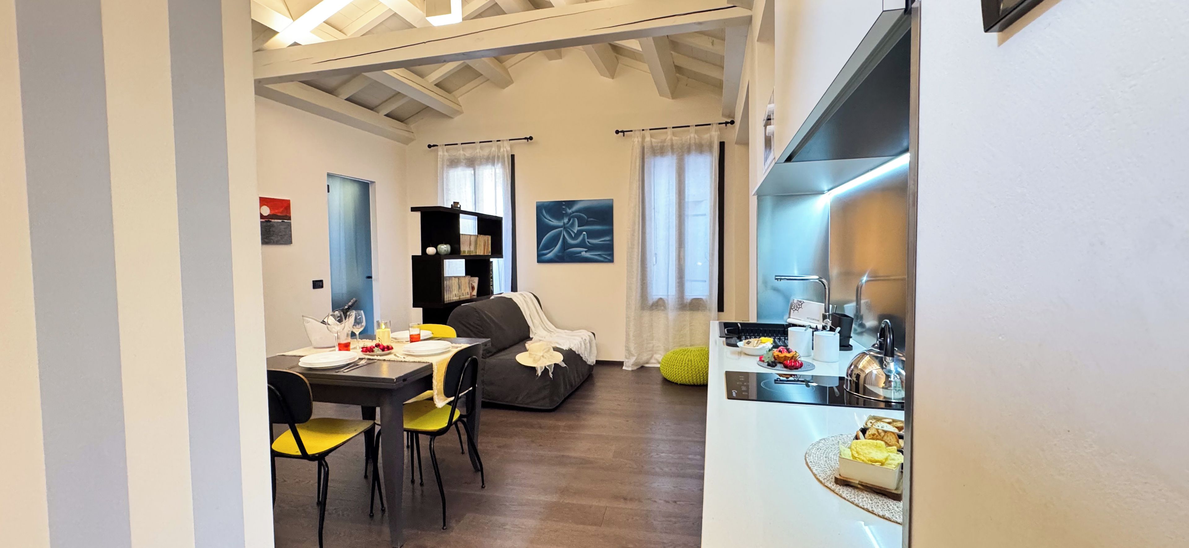 A modern living room with a dining area, a kitchen, and a dining table set with plates and cutlery.