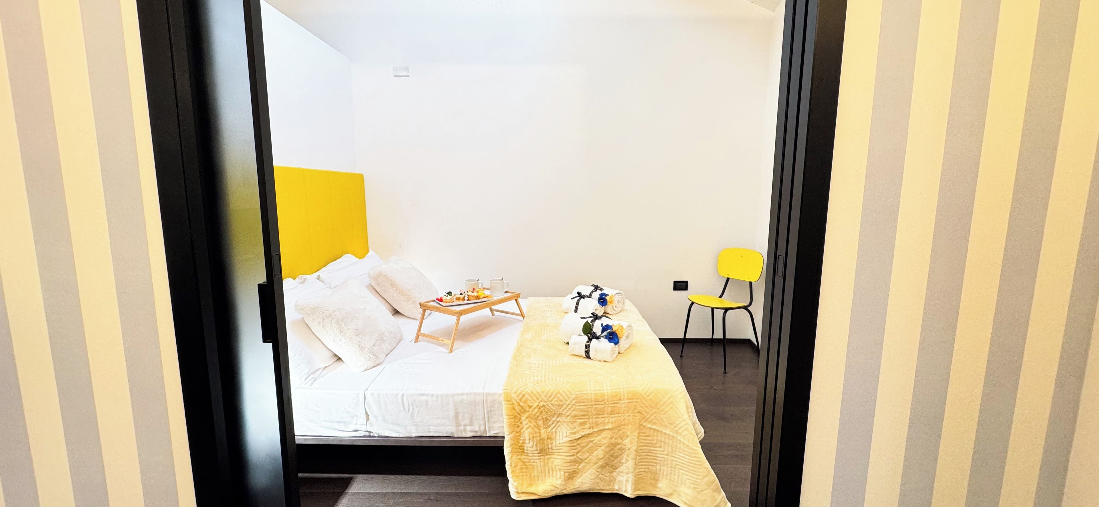 Ein Hotelzimmer mit Bett, einem kleinen Tisch mit Essensservit und einem Stuhl, sowie einem gelben Kopfteil.