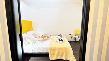 Ein Hotelzimmer mit Bett, einem kleinen Tisch mit Essensservit und einem Stuhl, sowie einem gelben Kopfteil.