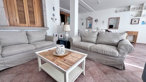 Una sala de estar con dos sofás grises, una mesa de centro blanca y una puerta de madera con contraventanas.