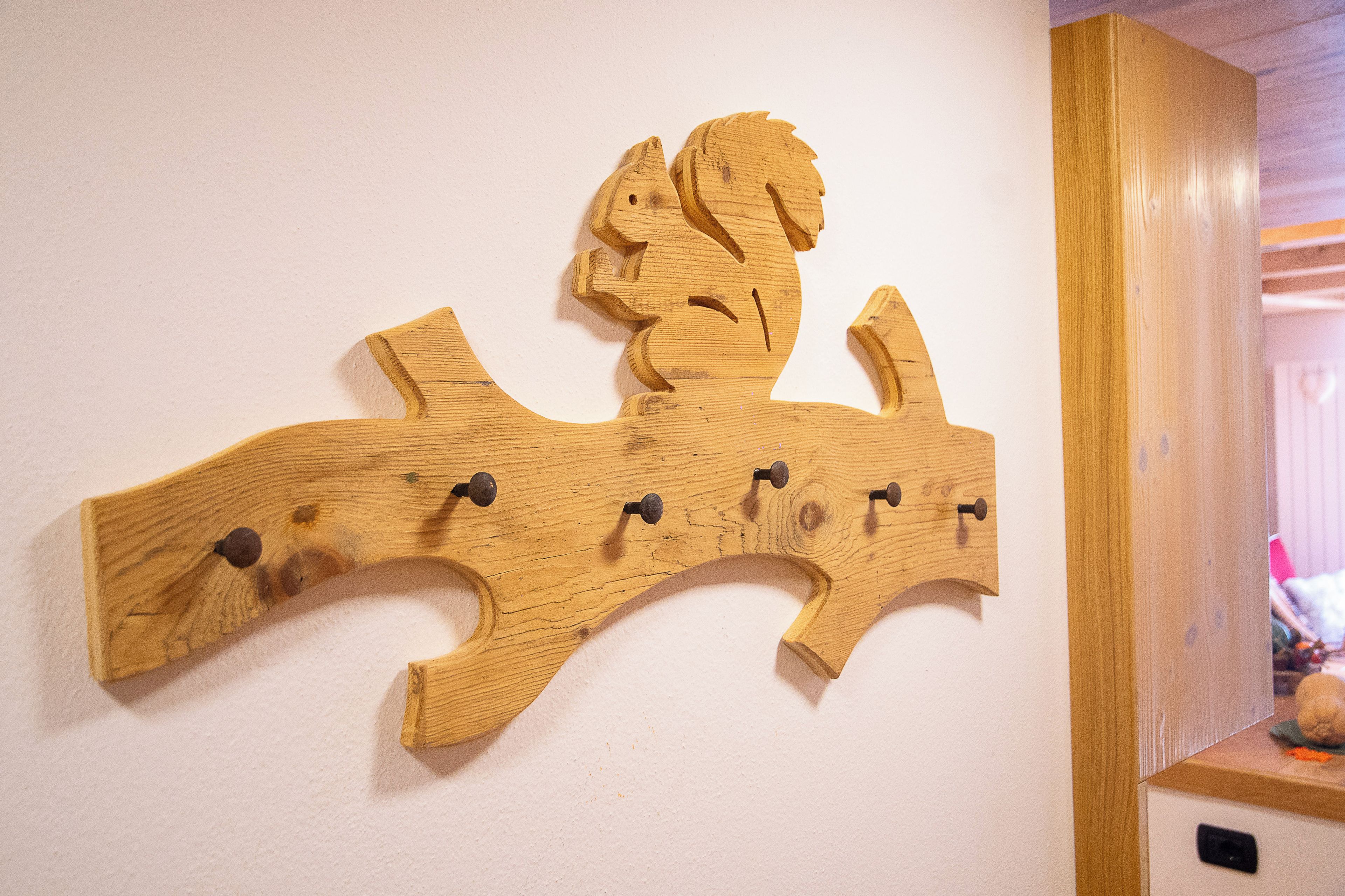 Un étagère en bois fixée au mur, dotée de crochets, probablement destinée à suspendre des objets, dans une pièce aux murs blancs et aux moulures en bois.
