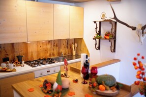 A kitchen with wooden cabinets, a gas stove, and a decorative shelf with pumpkins and a branch. - Appartamento Neve by Ca-sa Check (Aprica)