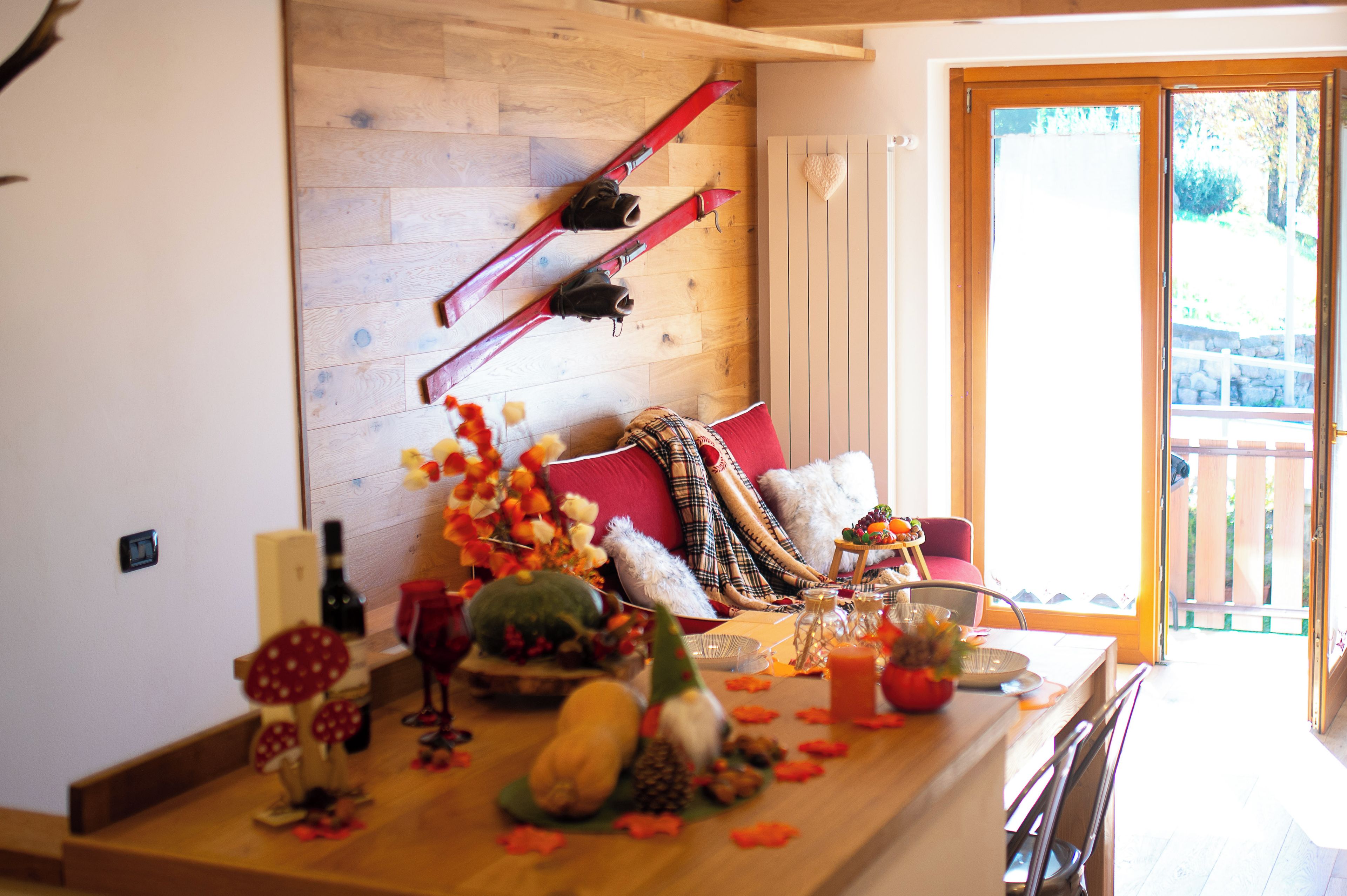 A cozy room with a wooden floor, a sofa with a plaid blanket, a dining table set with food and drinks, and a ski rack against the wall.
