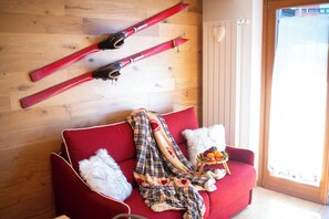 A red sofa with a plaid blanket, two white pillows, and a small fruit basket. - Appartamento Neve by Ca-sa Check (Aprica)