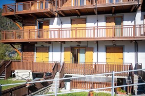 A multi-story building with wooden balconies, a staircase, and a small outdoor seating area. - Appartamento Neve by Ca-sa Check (Aprica)