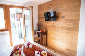 A hotel room with a wooden floor, a bed with a red blanket, a desk with a lamp, and a TV mounted on the wall. - Appartamento Neve by Ca-sa Check (Aprica)