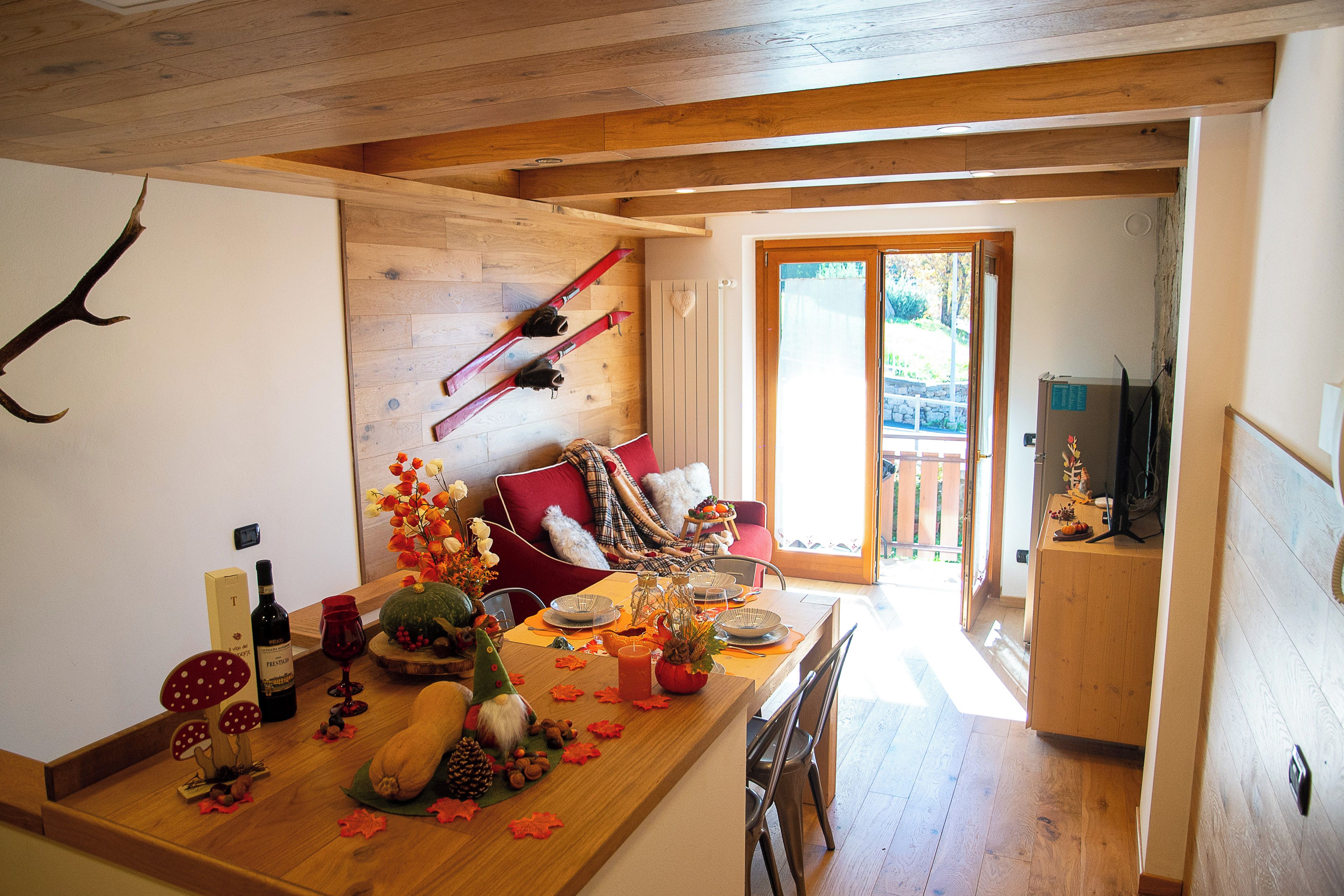 A dining area with a wooden table set for a meal, a ski rack on the wall, and a view of the outdoors through a glass door.