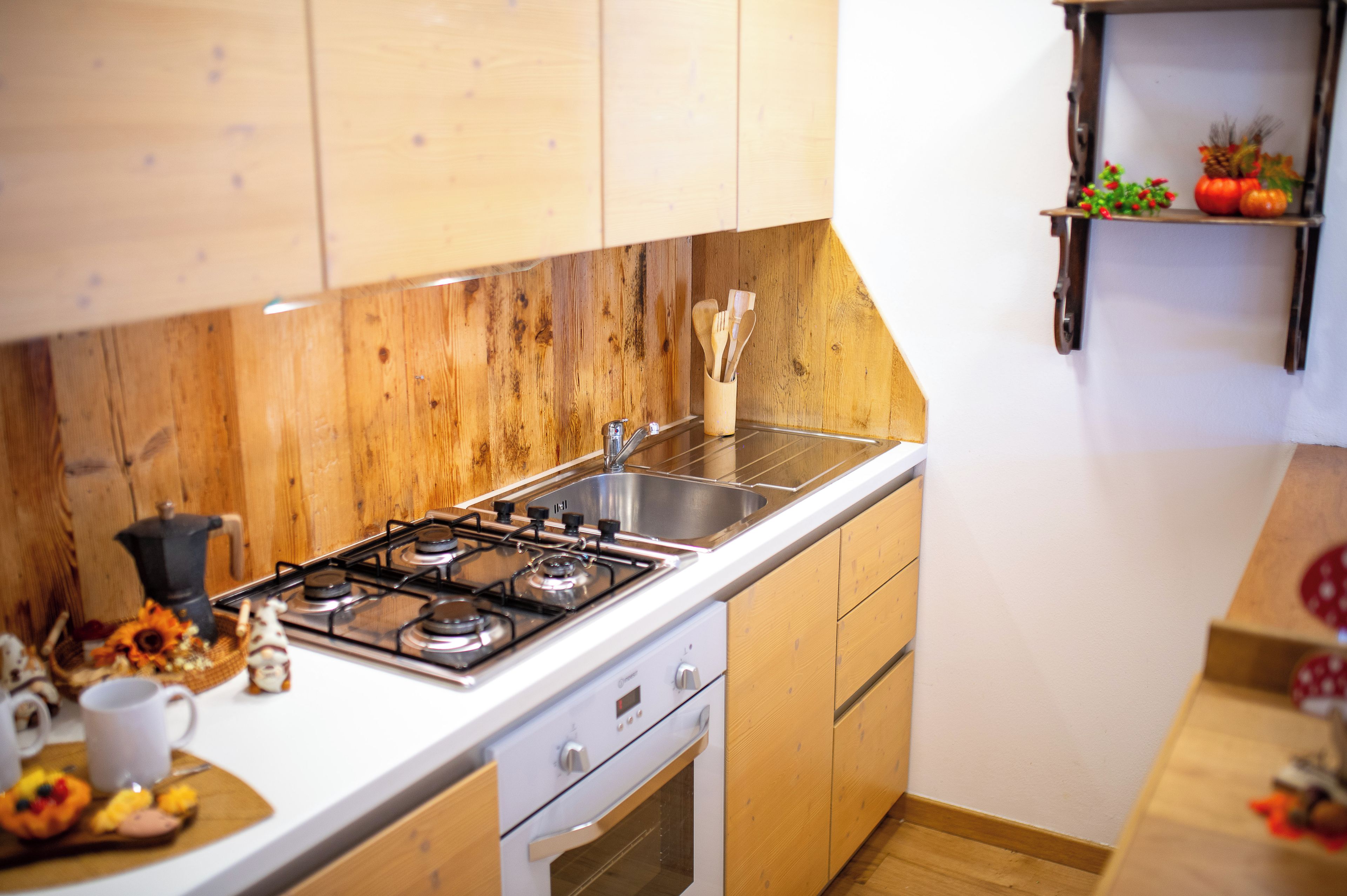 A kitchen with wooden cabinets, a stainless steel sink, a gas stove, and a small shelf with decorative items.