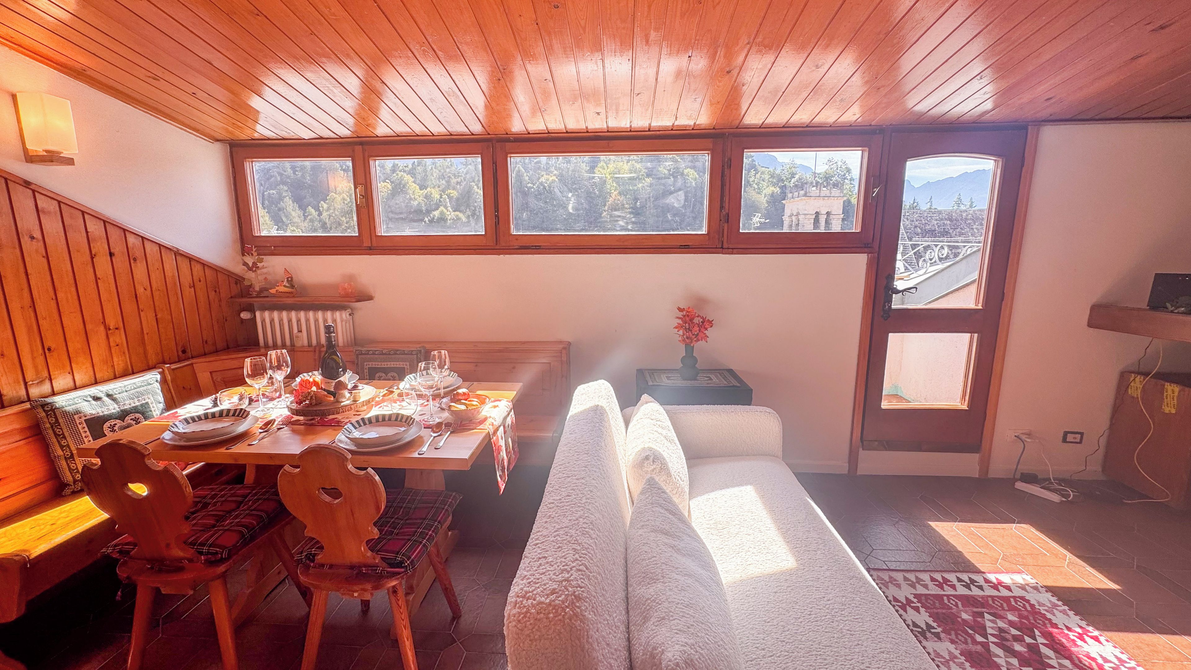 Un coin repas avec une table en bois dressée pour quatre personnes, un banc et une vue sur l’extérieur grâce à de grandes fenêtres.