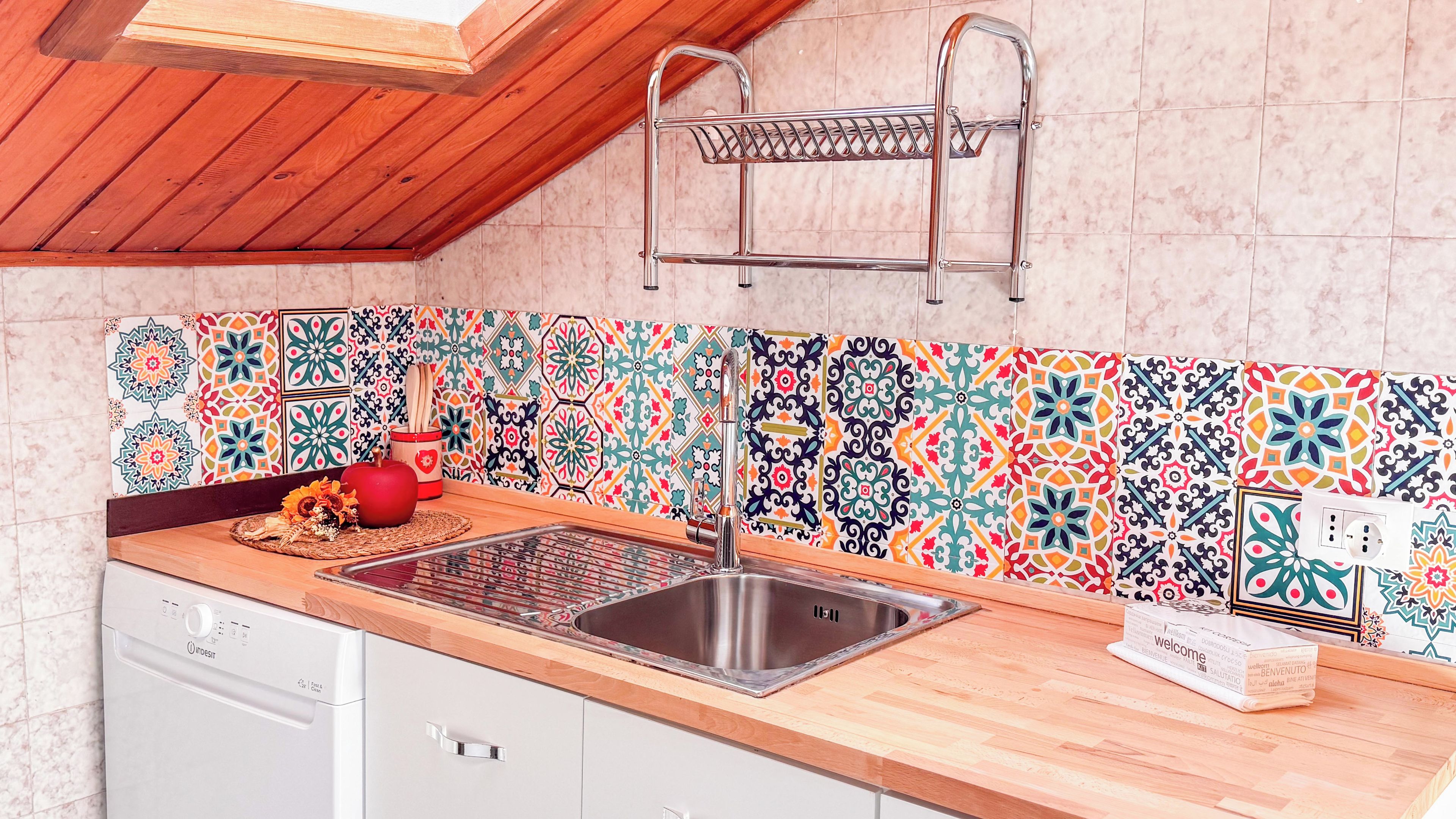 A kitchen with a wooden countertop, stainless steel sink, and colorful patterned backsplash.